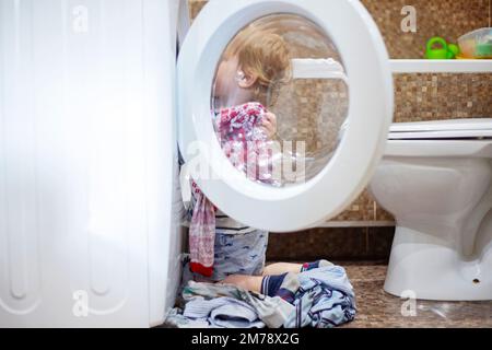 Child in bathroom with washing machine. Kid helping with family chores Stock Photo
