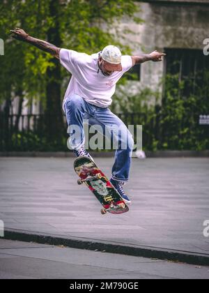 A vertical shot of a tattooed male doing a skateboard trick in New York City Stock Photo