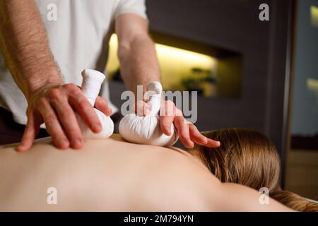Close up of woman lying on couch and getting herbal bag massage in spa Stock Photo