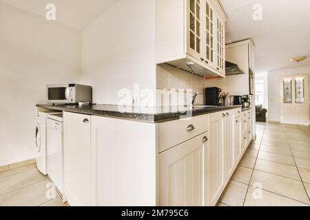 a kitchen area with white cabinets and black counter tops on the floor in front of the oven, microwave, toaster and dishwasher Stock Photo
