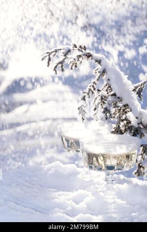 Two crystal glasses of sparkling wine or champagne cooling in snow on winter natural background with beautiful sunlight bokeh. Minimal creative composition with copy space. Holiday celebration concept. Stock Photo