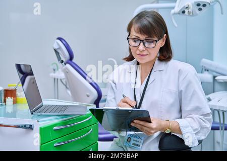 Doctor dentist working in office, using laptop, making notes on clipboard Stock Photo