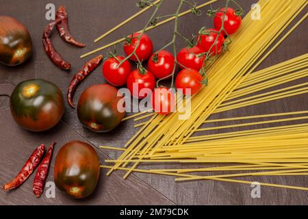 Spaghetti, cherry tomato sprig and whole brown tomatoes. Top view. Brown background. Stock Photo