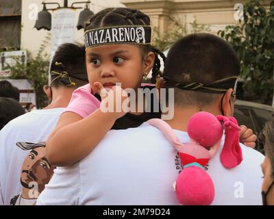 Manila, Philippines. 8th Jan, 2023. A father carries a child wearing a Black Nazarene headband. Catholic devotees flock to Quiapo Church in Manila to express their devotion to the Black Nazarene, a life-sized image of dark skinned, kneeling Jesus Christ carrying the cross. A day before it's feast on January 9. This festive activity was put on hold for two years because of the COVID-19 pandemic. Credit: ZUMA Press, Inc./Alamy Live News Stock Photo