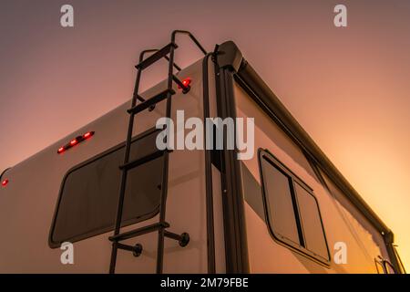Closeup of a Rear Part of Modern RV with Steps to the Roof in the Light of Setting Sun. Motorhome Traveling Theme. Stock Photo