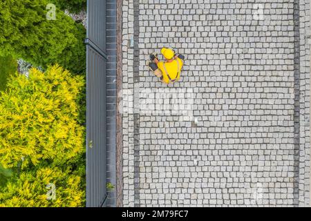 Aerial View of Contractor Finishing Building of Granite Brick Driveway Along the Fence. Domestic Yard Design and Construction Theme. Stock Photo