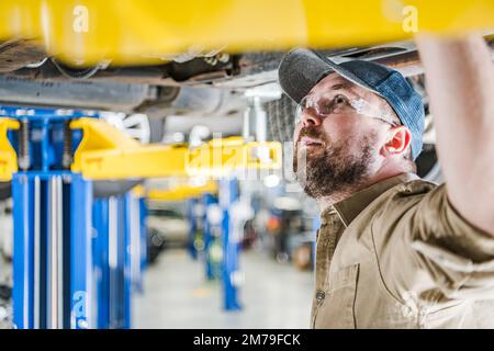 Closeup of Caucasian Middle Aged Mechanic Inspecting Undercarriage of the Vehicle Secured on Car Lift. Professional Automobile Repair Shop. Stock Photo