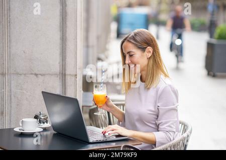 Happy female freelancer working on netbook in outdoor cafeteria Stock Photo