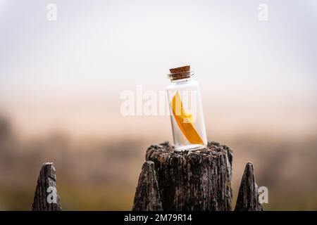 Miniature origami ship in glass bottle standing on a wooden fence at sunrise Stock Photo