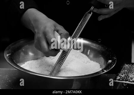 chef grating parmesan cheese with fine grater  in close up in kitchen Stock Photo