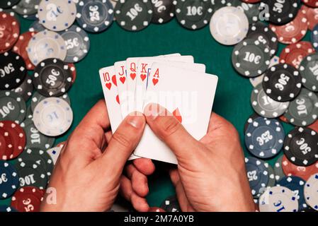 Royal flush in the game of poker in the hands of the player on the background of a green table with gaming chips in the casino Stock Photo