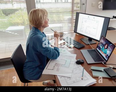 Focused mature woman engineer constructor works on project from home office using computer Stock Photo