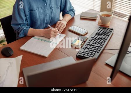 Close up of woman hands taking notes while working in cozy home office remotely Stock Photo