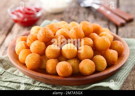 Fresh round baked Duchess potatoes or croquettes on wooden plate, ketchup and mayonnaise in the back (Selective Focus) Stock Photo