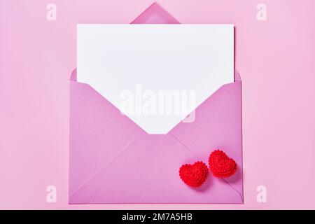 Greeting card mockup, white blank card in an envelope and knitted red hearts. Stock Photo