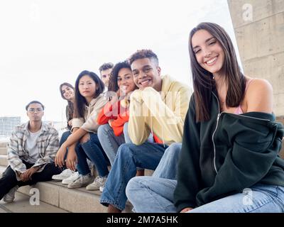 Diverse teenage friends looking at camera smiling sitting on stairs in a city Stock Photo
