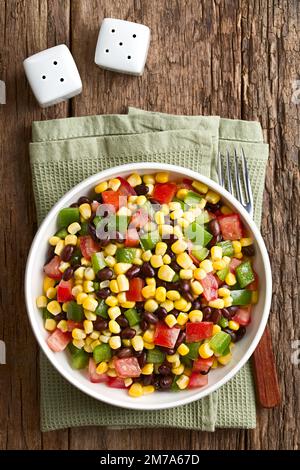 Mexican style colorful fresh vegetable salad made of beans, corn, tomato and bell pepper served in bowl, photographed overhead on wood Stock Photo