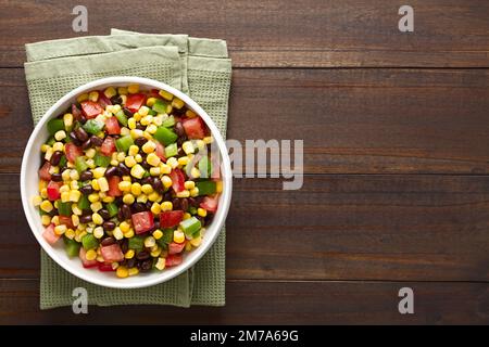 Mexican style colorful fresh vegetable salad made of beans, corn, tomato and bell pepper served in bowl, photographed overhead on dark wood Stock Photo