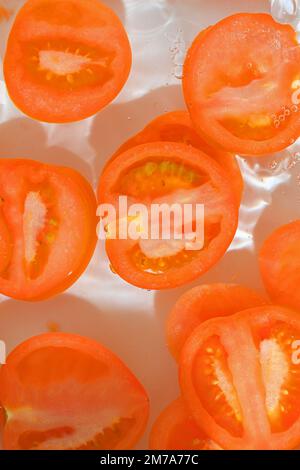 Close-up fresh slices of tomato on white background. Slices of tomato in sparkling water on white background, close-up. Vertical image. Stock Photo
