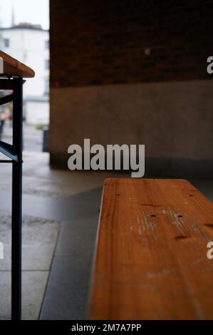 Wooden bench and metal table leg with blurred background and foreground in covered urban street setting Stock Photo