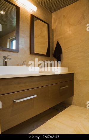White rectangular porcelain sinks and brown wooden vanity in his and her bathroom on upstairs floor inside modern cubist style home. Stock Photo
