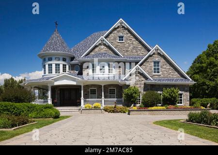 Elegant modern grey stone with white trim and blue roof Victorian style home and paving stone alley in summer. Stock Photo