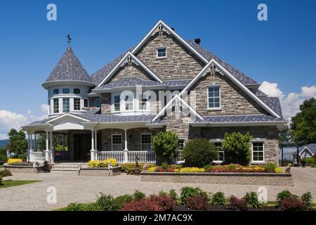 Elegant modern grey stone with white trim and blue roof Victorian style home and paving stone driveway in summer. Stock Photo