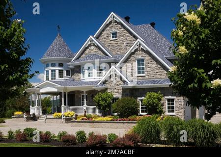 Elegant modern grey stone with white trim and blue roof Victorian style home and paving stone driveway in summer. Stock Photo