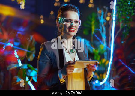 Portrait of happy modern business woman with futuristic goggles using tablet PC in metaverse. Stock Photo