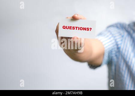 Man holding a white business card with text, Questions? Stock Photo