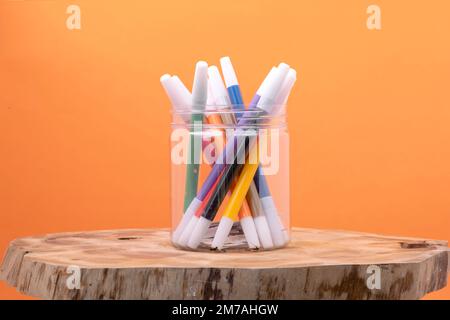 Plastic container with a bunch of colored markers on wood on orange background Stock Photo