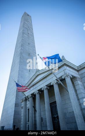 Bunker Hill Monument in Charlestown with obelisk and lodge along with United States flag and New England flag flown on the battlefield at Breed's Hill Stock Photo