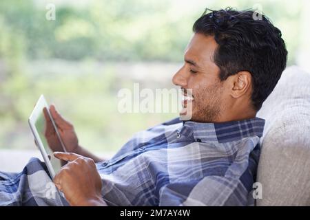 Enjoying some downtime with his digital tablet. a young man using his tablet while relaxing at home. Stock Photo