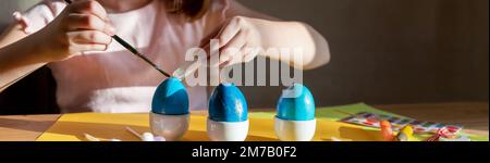 Child paints easter egg. Creativity with children. girl's hands with eggs on the background of a table with paints, brushes, eggs, holiday flags.do-it Stock Photo