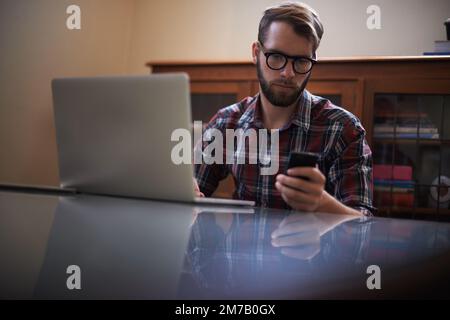 Using all the latest tech. a handsome young hipster working on a laptop. Stock Photo