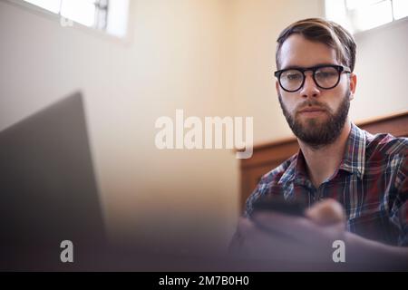 Using all the latest tech. a handsome young hipster working on a laptop. Stock Photo