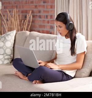 OMG Thats unbelievable. An attractive young woman watching something on her laptop at home. Stock Photo