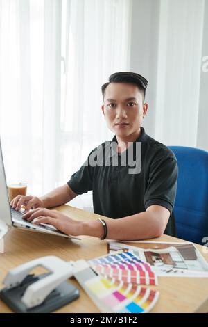 Portrait of young Vietnamese interior designer working on laptop at his office table Stock Photo