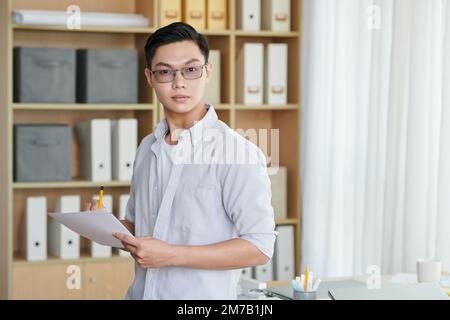 Portrait of young architect in glasses filling document with measurements for construction project Stock Photo