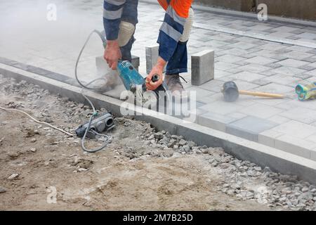 Construction of a footpath from paving slabs. The worker cuts paving slabs for subsequent even laying. Copy space. Stock Photo