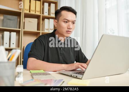 Portrait of frowning serious architect working on laptop at office desk Stock Photo