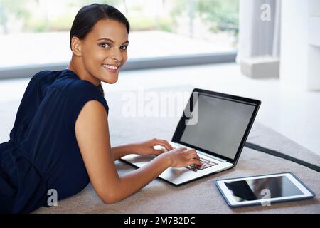Ive got the tech I need at my fingertips. an attractive young woman using her laptop and tablet while relaxing on the floor at home. Stock Photo