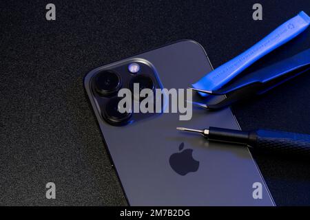 South Tyrol, Italy - Jan. 7. 2023: Repair tools on top of Apple iPhone Pro. Screwdriver and Tweezers on Smartphone for repair Stock Photo