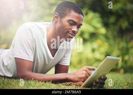 Online in the open air. a young man lying on the grass and using a digital tablet. Stock Photo
