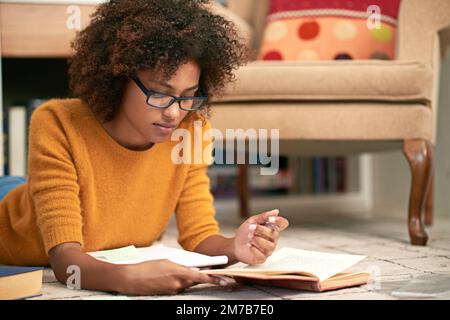 Focused on her studies. a young woman lying on the floor while studying. Stock Photo