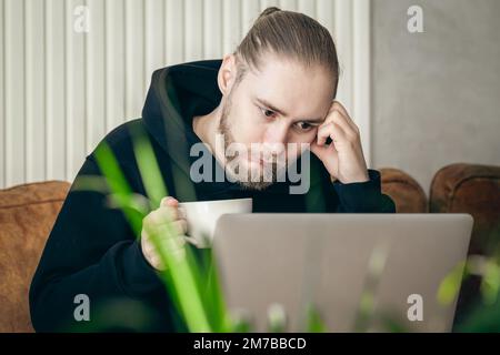 Tired young man working on a laptop with a cup of coffee. Stock Photo
