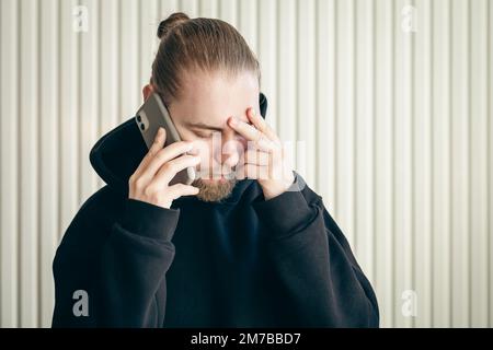 A young man talking on smartphone and holding his head, concept of problem. Stock Photo