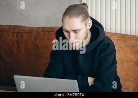 An attractive young man with a beard is working on a laptop. Stock Photo