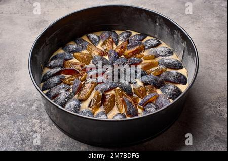 Homemade pie or tart with plums in baking dish on marble wooden background. Close up Stock Photo