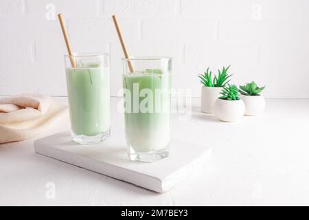 a large glass of matcha latte green tea and straw on a white marble board  against a backdrop of textured wall and plants in pots. Detox. 17567235  Stock Photo at Vecteezy